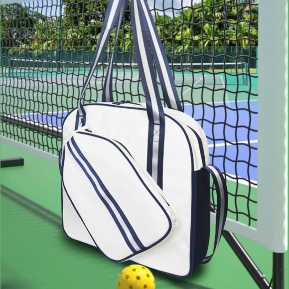 White pickleball tote bag with handheld straps holding two paddles against blue sky outdoor scene
