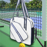 White pickleball tote bag with handheld straps holding two paddles against blue sky outdoor scene